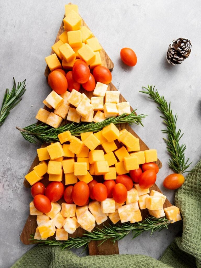 Cheese cubes and cherry tomatoes arranged in a tree shape with rosemary sprigs on a wood surface.