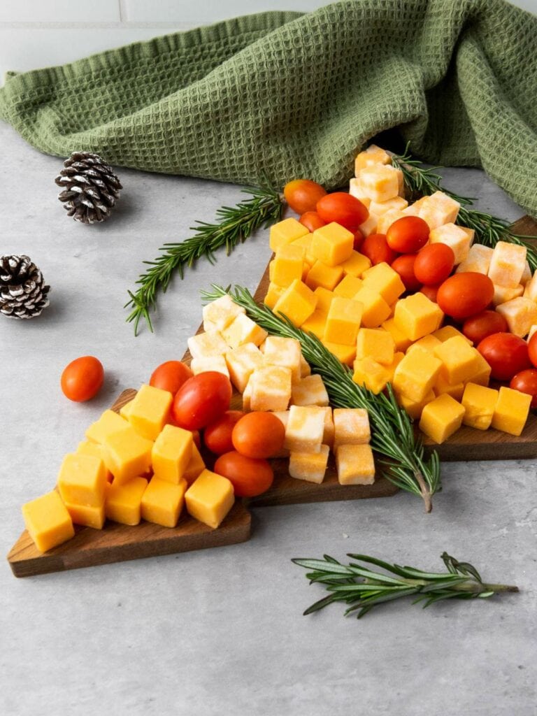 Cheese cubes, cherry tomatoes, and rosemary arranged in the shape of a Christmas tree on a wooden board.