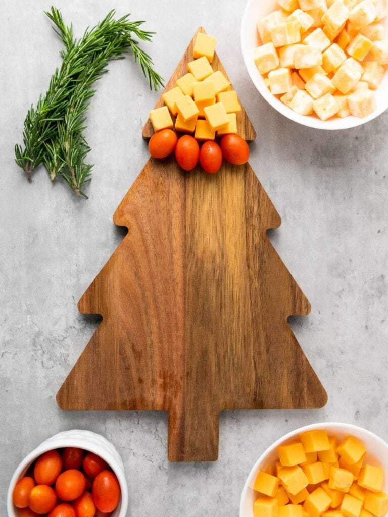 Wooden tree-shaped board with cherry tomatoes and cheese cubes.