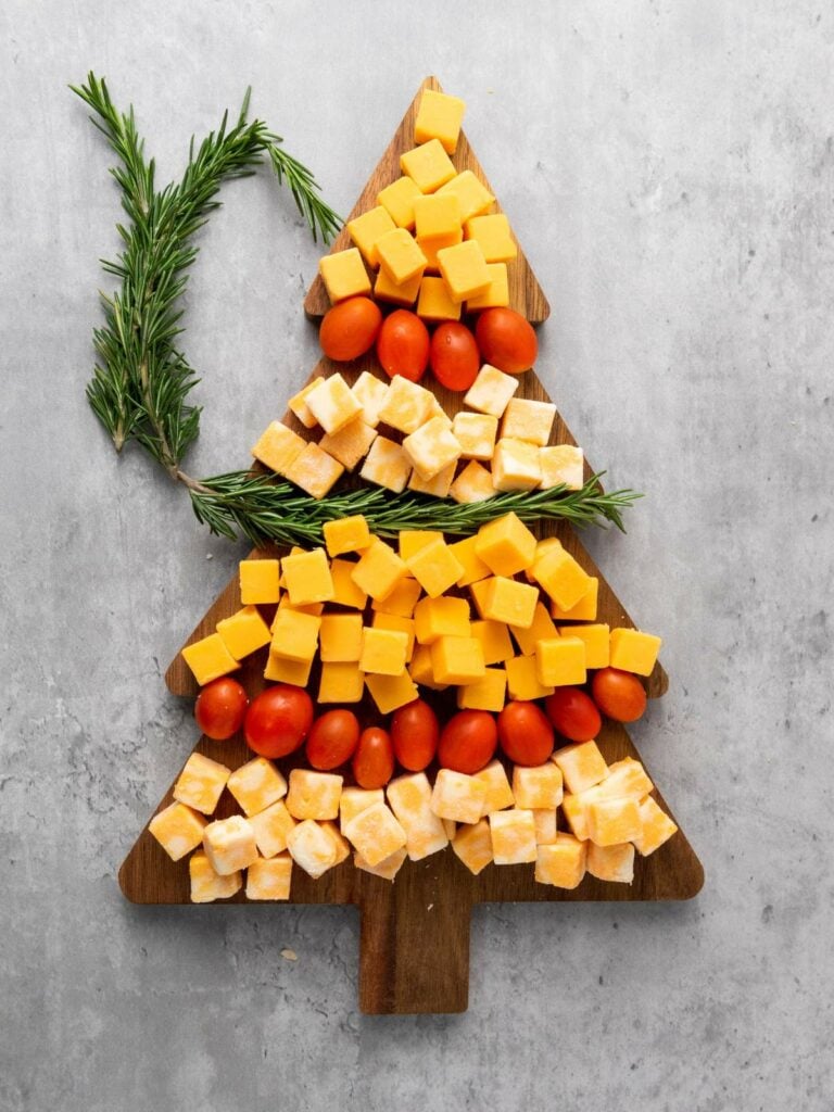 Cheese cubes and cherry tomatoes arranged in a tree shape on a wooden board, garnished with rosemary.