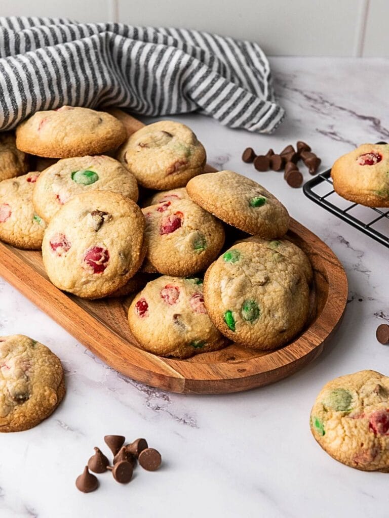 A wooden tray with assorted cookies, some with colorful candies, on a marble surface.