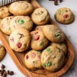 A wooden tray with assorted cookies containing chocolate chips and colorful candies on a marble surface.