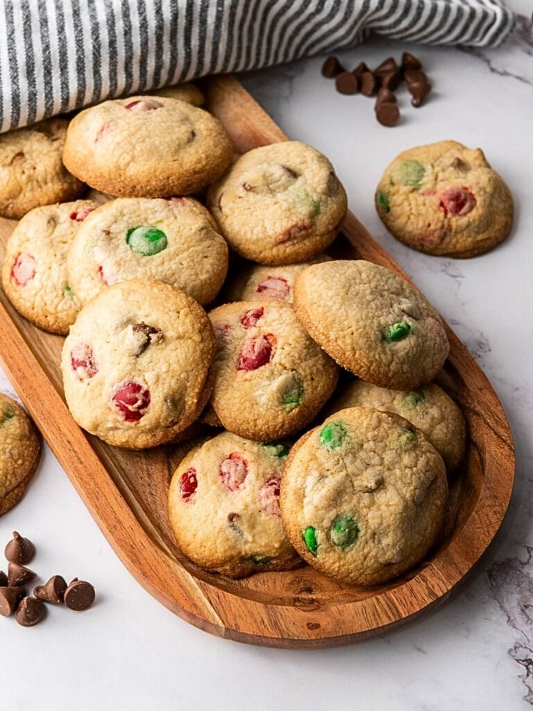 A wooden tray with assorted cookies containing chocolate chips and colorful candies on a marble surface.