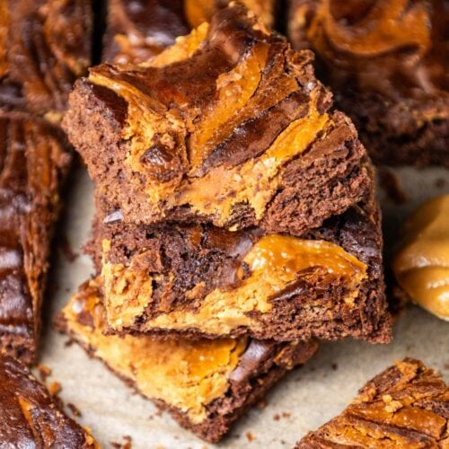 Stack of brownies with swirled peanut butter on top, placed on parchment paper.