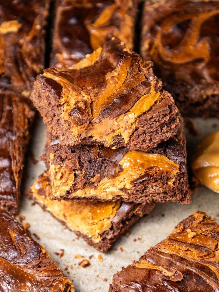 Stack of brownies with swirled peanut butter on top, placed on parchment paper.