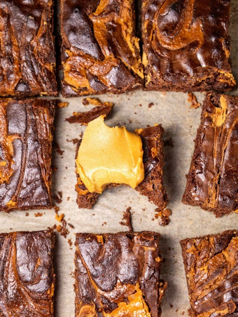 Nine peanut butter brownies on parchment paper. One brownie is partially eaten.