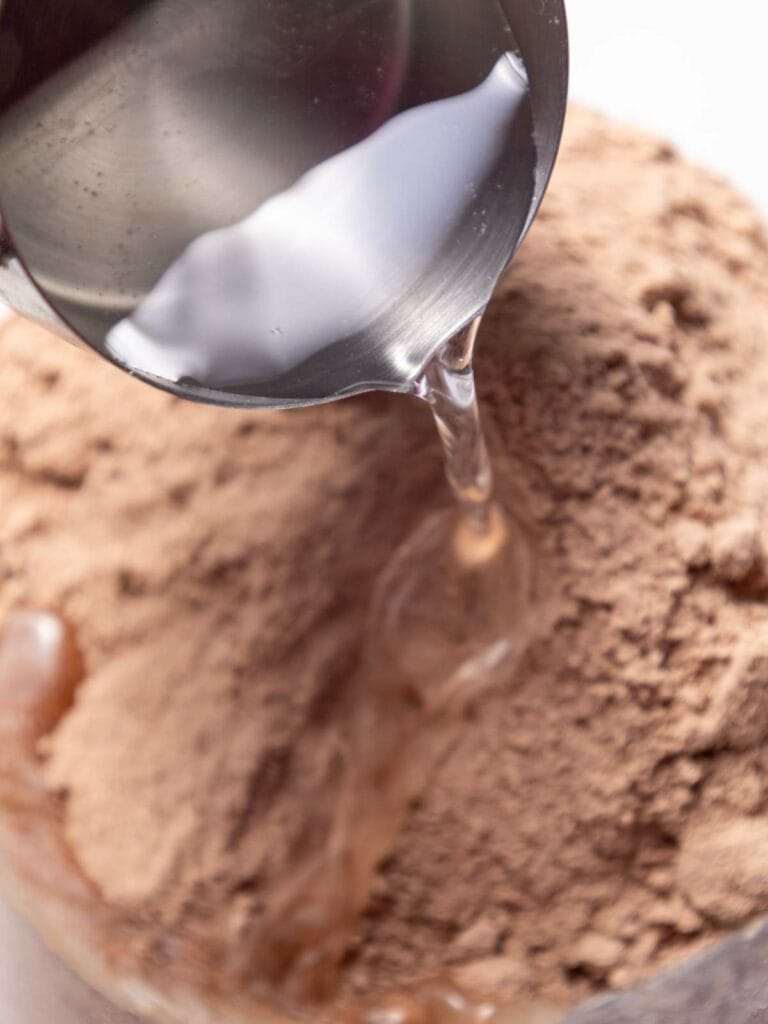 Pouring water into a bowl of brown powder for mixing.