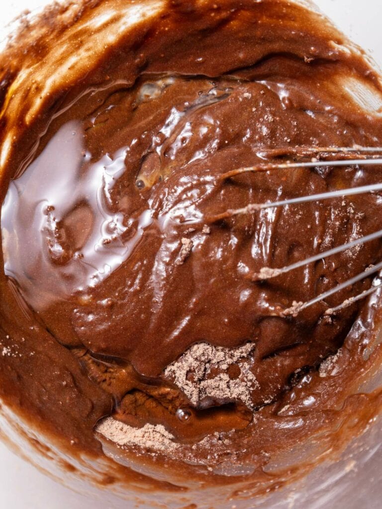 A whisk mixes thick chocolate batter in a bowl.