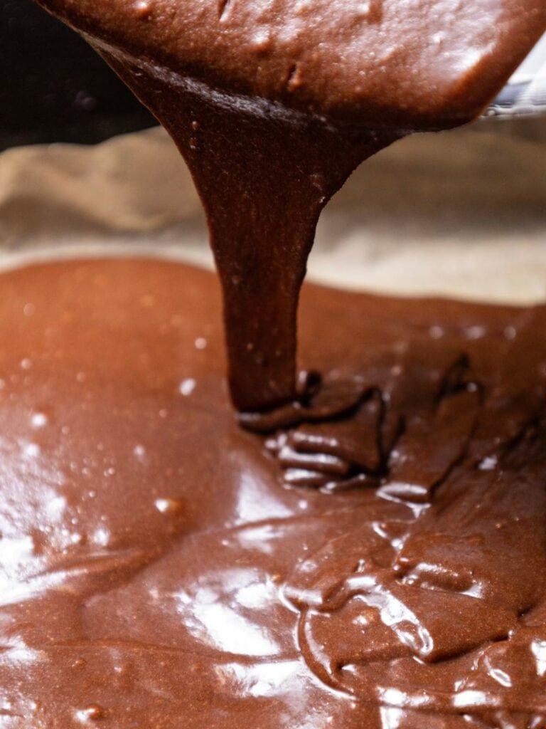 Thick chocolate brownie batter being poured onto a baking sheet.