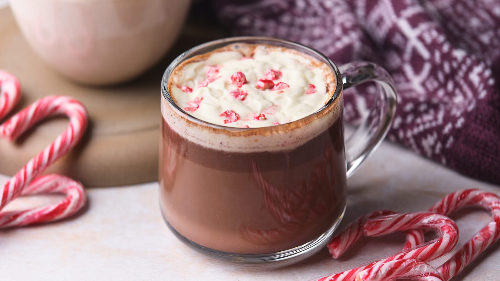 A glass mug of hot chocolate topped with whipped cream and crushed candy canes.