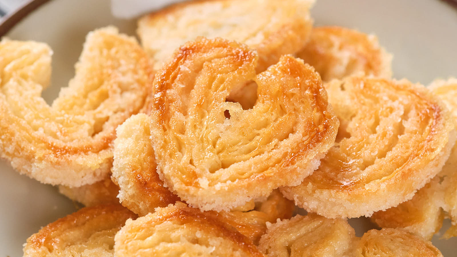 A plate of golden, heart-shaped puff pastry palmiers with a sugar coating.