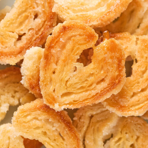 Close-up of golden-brown, heart-shaped puff pastries, showing flaky texture and sugar coating.