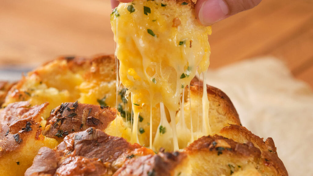 A piece of cheesy garlic bread being pulled apart, showing melted cheese and herbs.