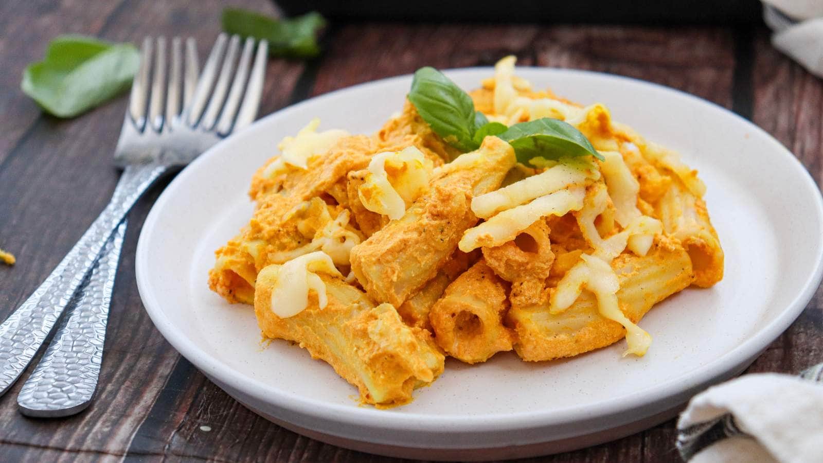 A plate of pumpkin pasta with creamy sauce and melted cheese, garnished with fresh basil.