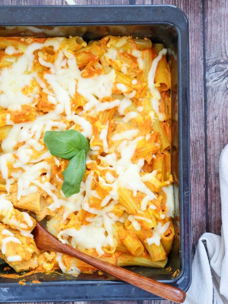 Pumpkin pasta with melted cheese and a basil garnish in a rectangular pan with a wooden spoon.