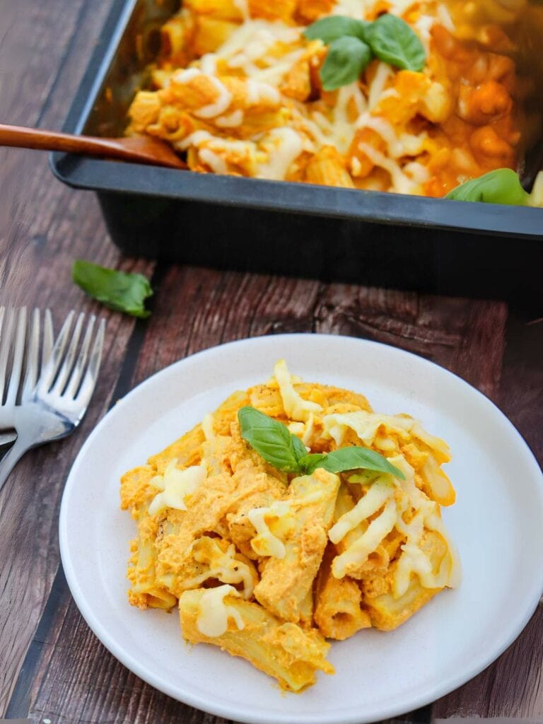 Plate of pumpkin pasta with cheese and basil leaves, with more pasta in a baking dish in the background.