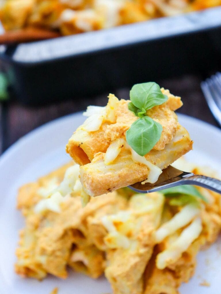 Close-up of a fork holding a bite of pumpkin pasta with sauce, topped with fresh basil.