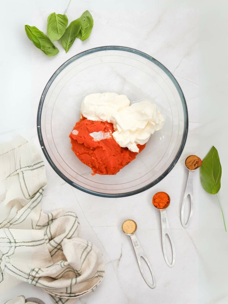 A glass bowl with cream and pumpkin puree on a marble surface.