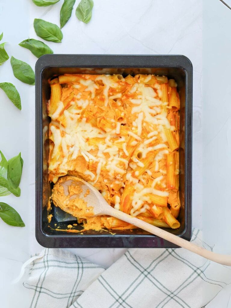 A baked pasta dish with melted cheese in a square pan, topped with a wooden spoon.