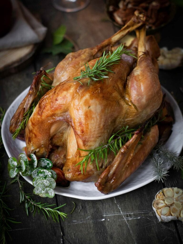 Roasted turkey on a white plate, garnished with fresh rosemary and lemon slices, on a wooden table.