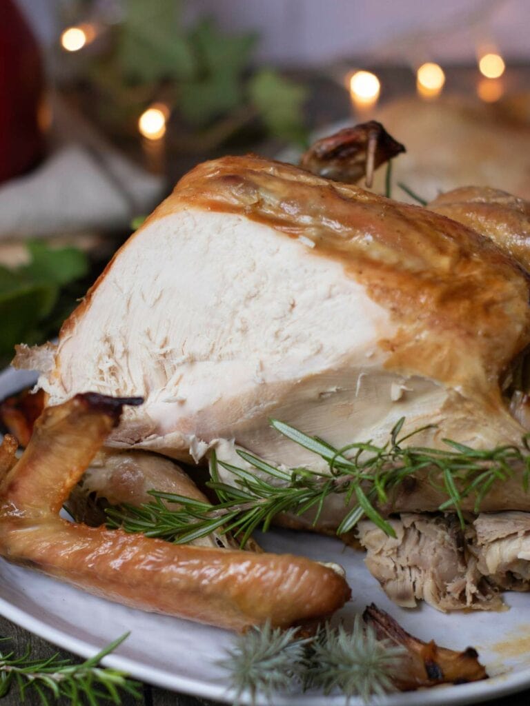 Roast turkey breast on a plate, garnished with rosemary sprigs.