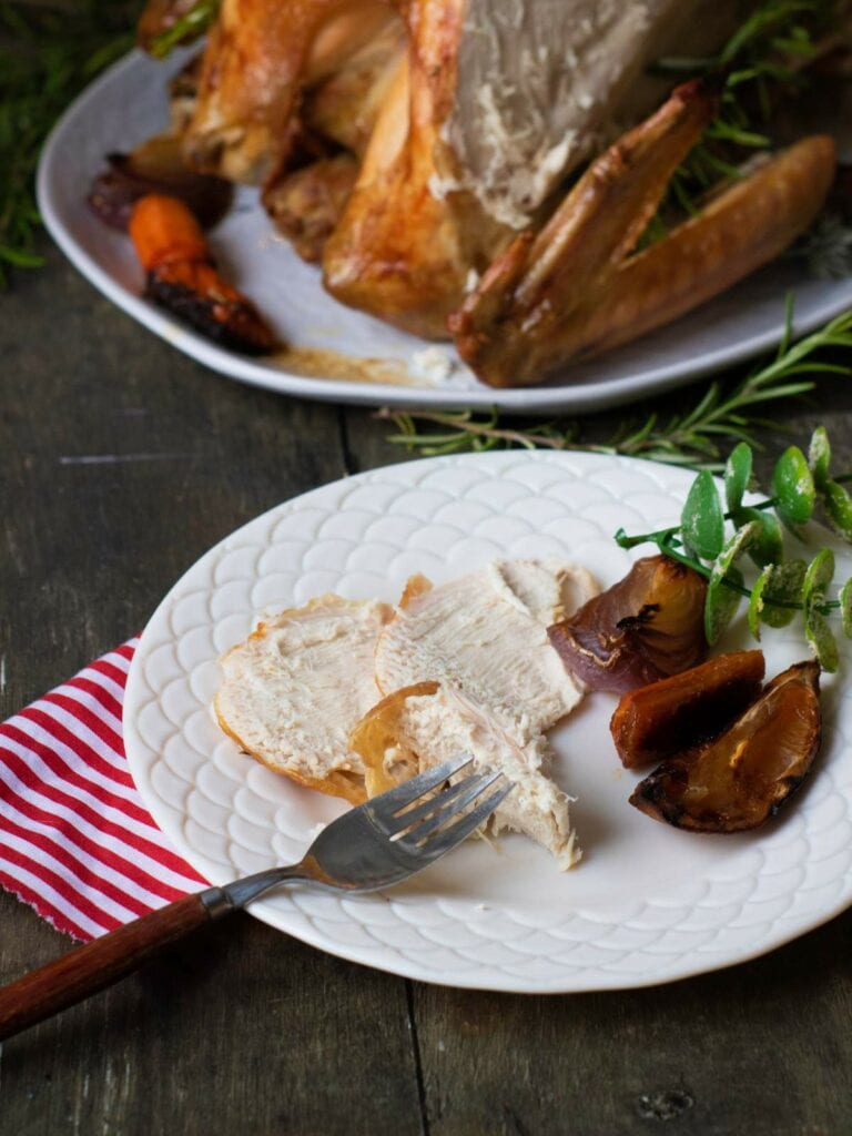 A white plate with slices of cooked turkey, roasted vegetables, and herbs.