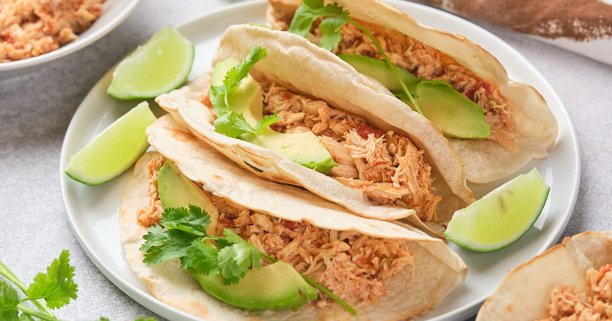 Close-up of shredded chicken with vegetables in a pan, being stirred with a wooden spoon.