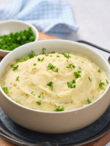 A bowl of mashed potatoes topped with chopped parsley.