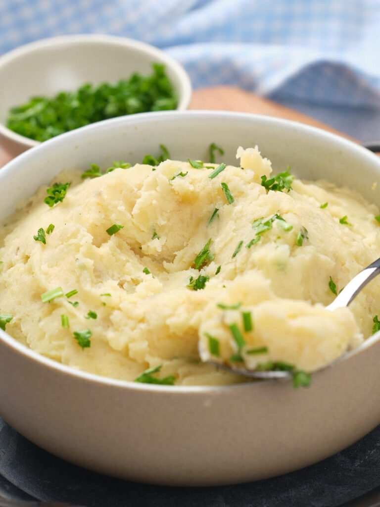 A bowl of mashed potatoes with chopped herbs and a spoon.