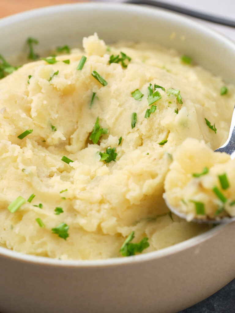 A bowl of mashed potatoes garnished with chopped parsley and a spoon resting on the side.