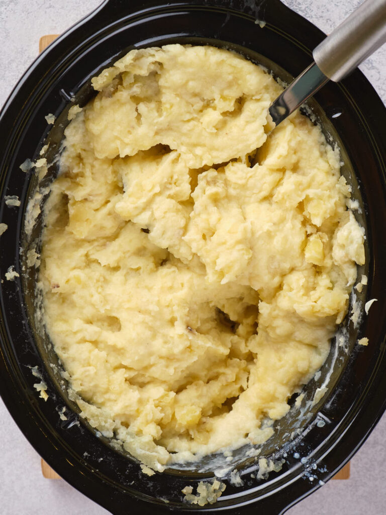 Creamy mashed potatoes in a black oval dish with a serving spoon.