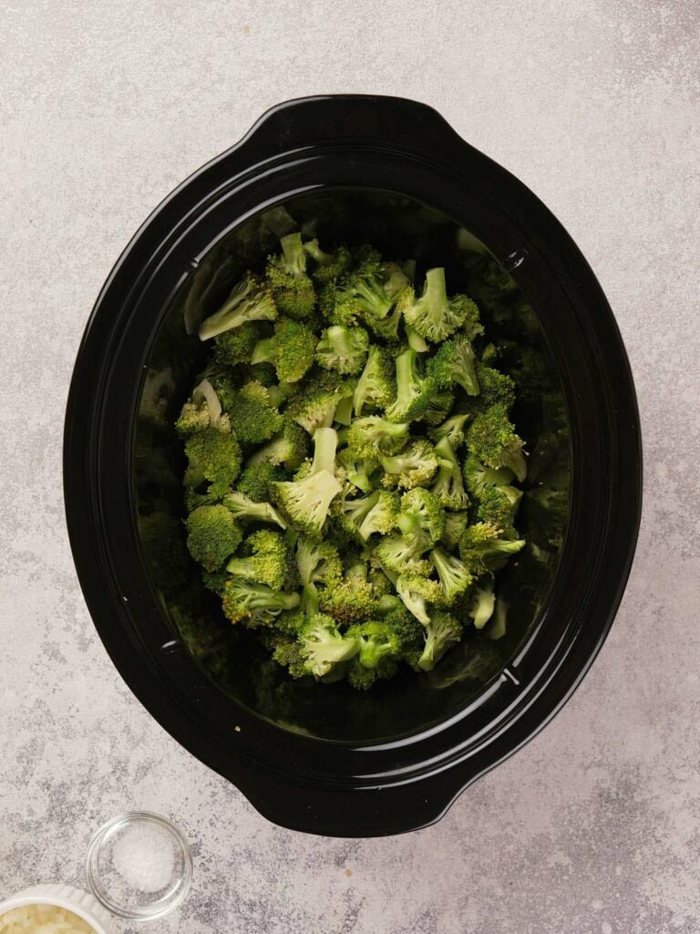 Top view of chopped broccoli in a black slow cooker on a light gray surface.