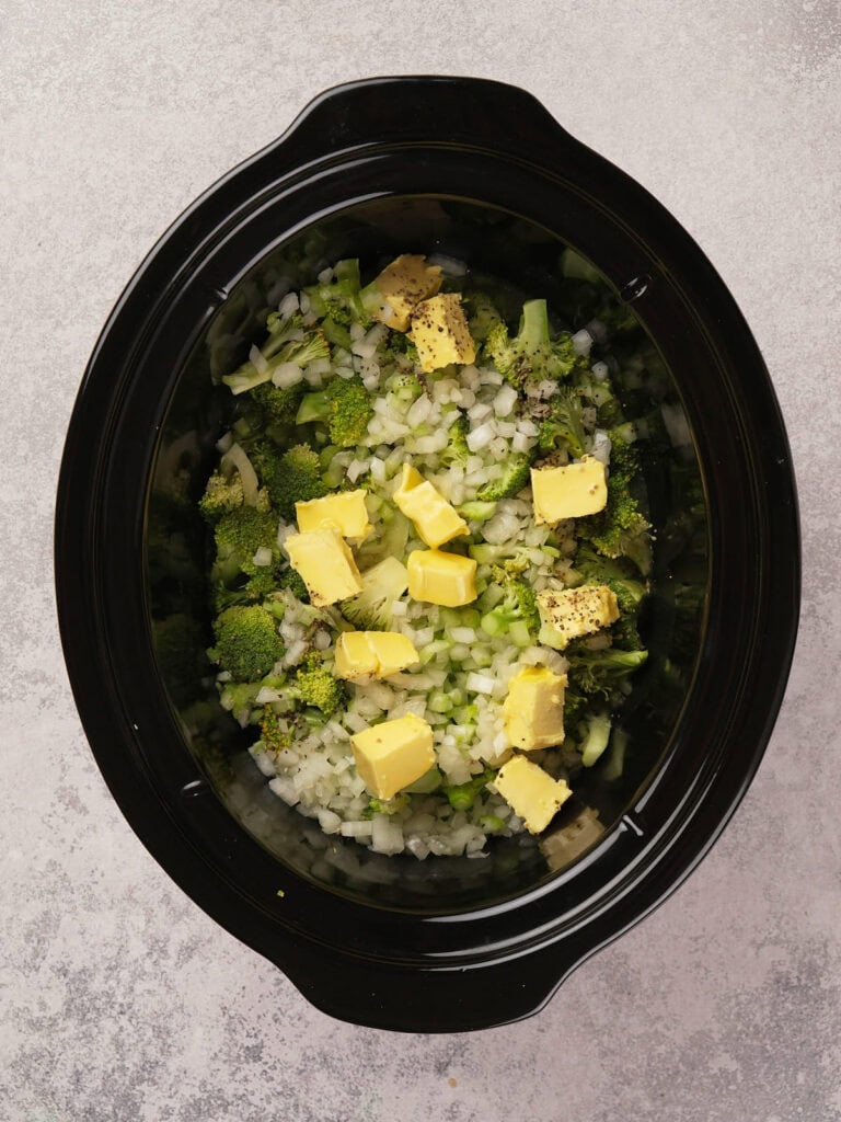 Crock pot with chopped broccoli, onions, and butter pieces.