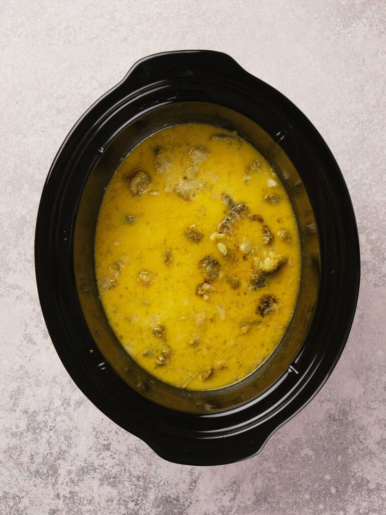 A black slow cooker filled with yellow curry containing chunks of meat and vegetables.