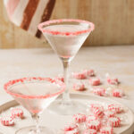 Two candy cane martini on a tray surrounded by wrapped peppermint candies.