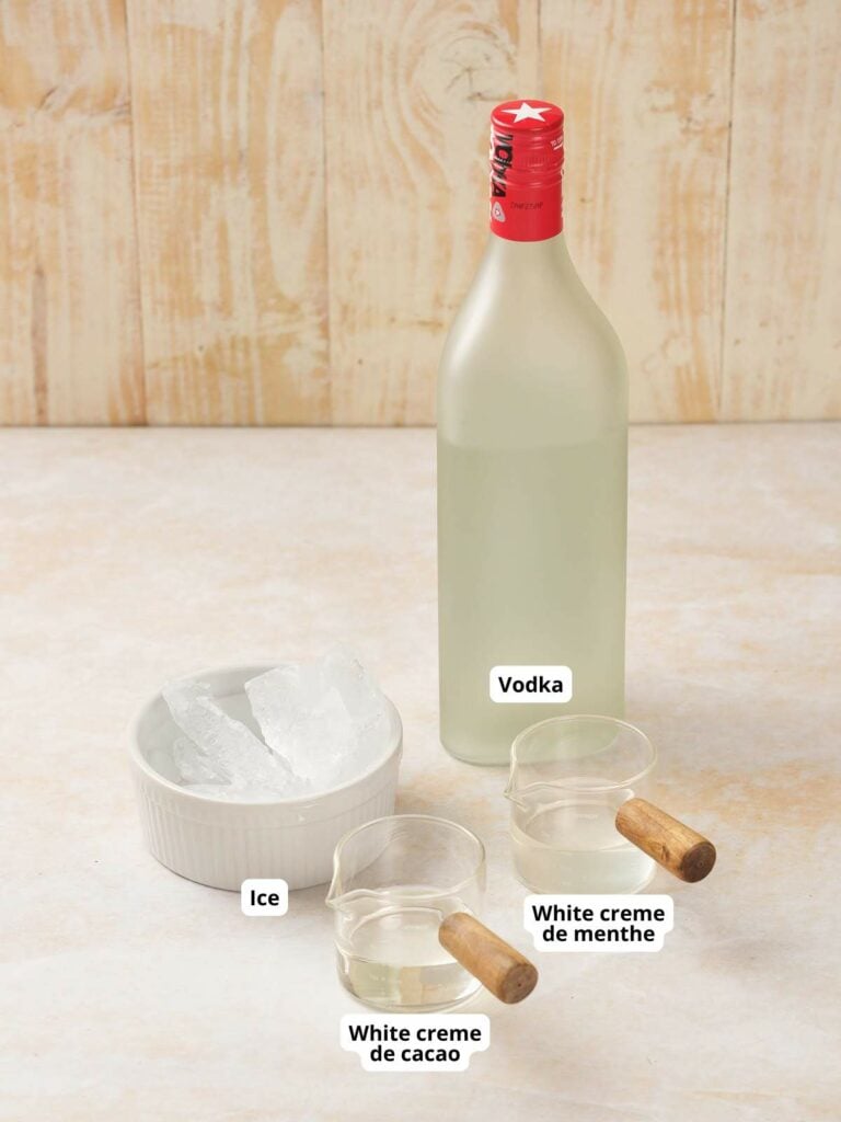 A bottle of vodka, a bowl of ice, and two labeled bottles of white crème de cacao and white crème de menthe.