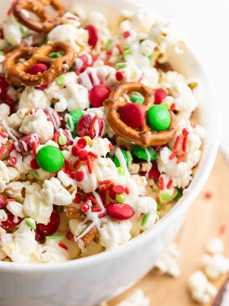 A bowl of popcorn mixed with pretzels, red and green candies, and festive sprinkles.