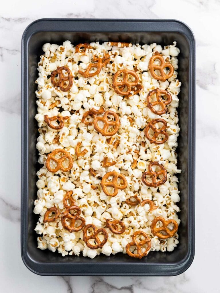 A gray rectangular pan filled with popcorn and pretzels on a marble surface.