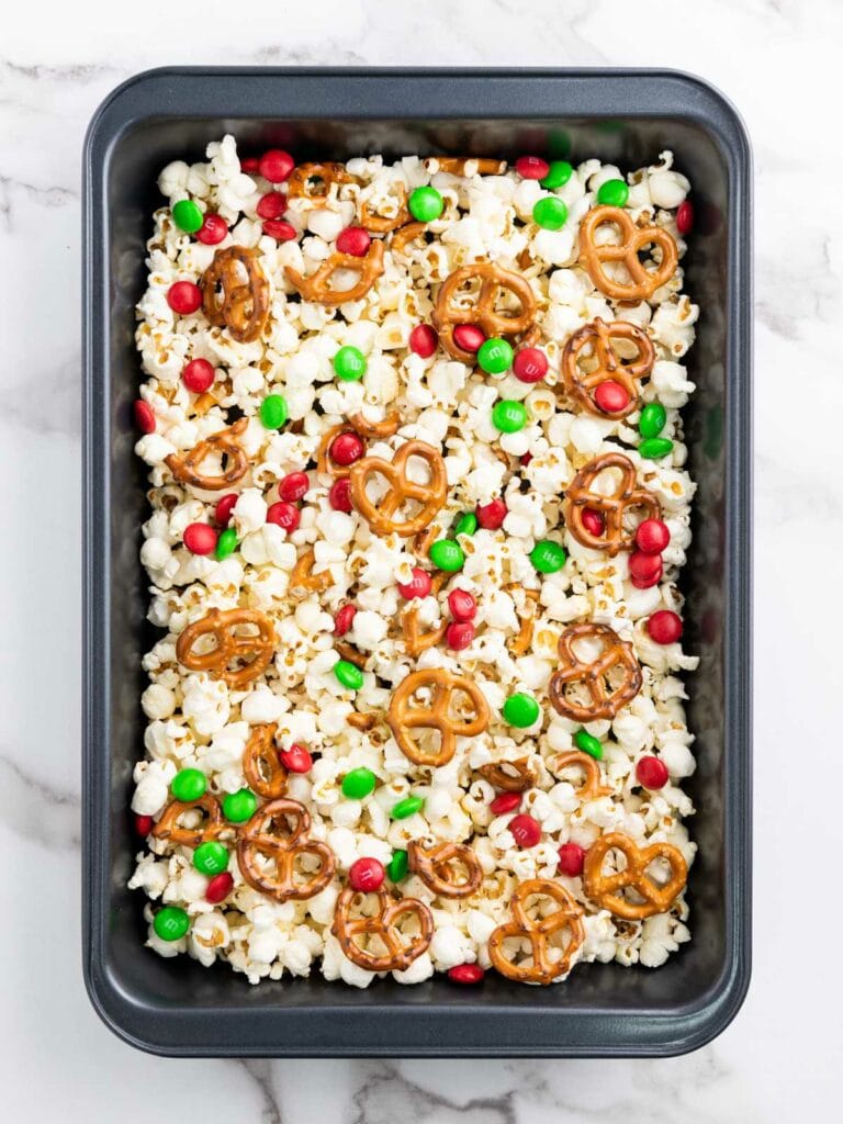 A baking tray filled with popcorn, pretzels, and red and green candy-coated chocolates.