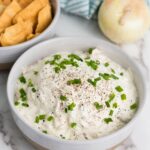 A bowl of creamy french onion dip topped with chopped green onions and pepper.