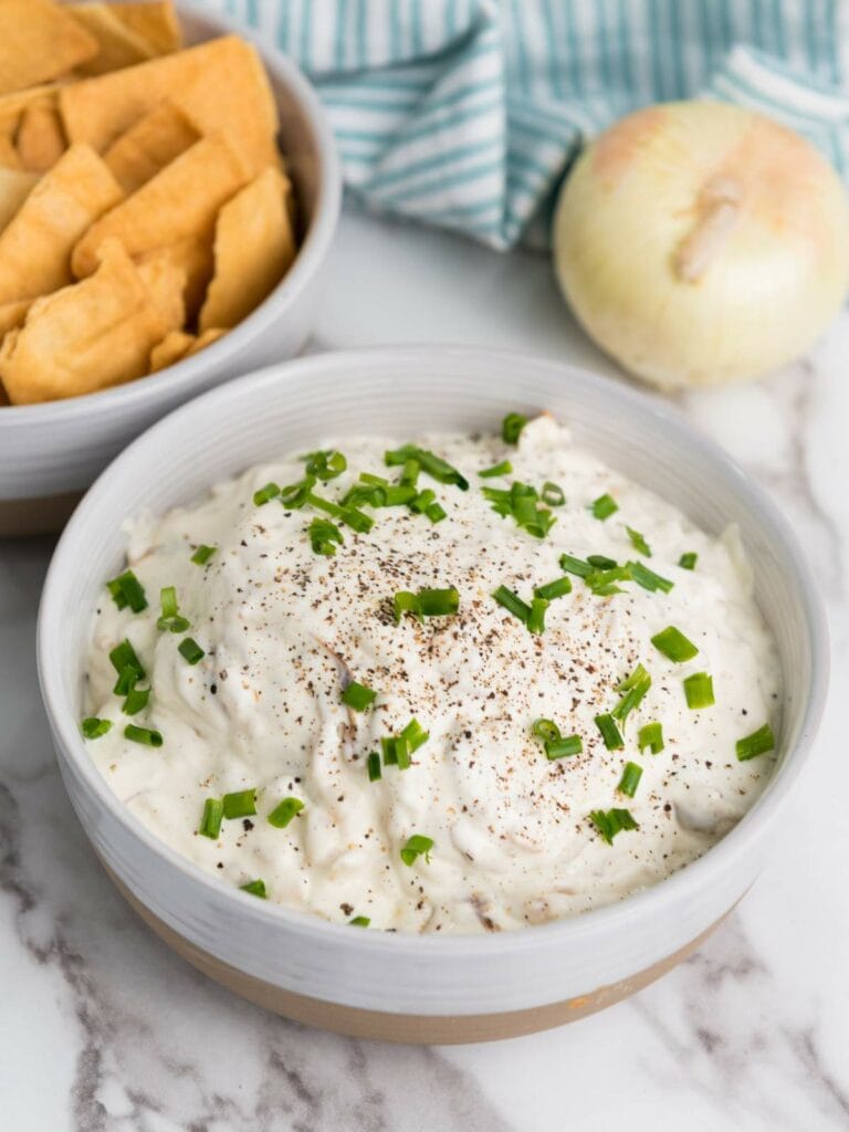 A bowl of creamy french onion dip topped with chopped green onions and pepper.