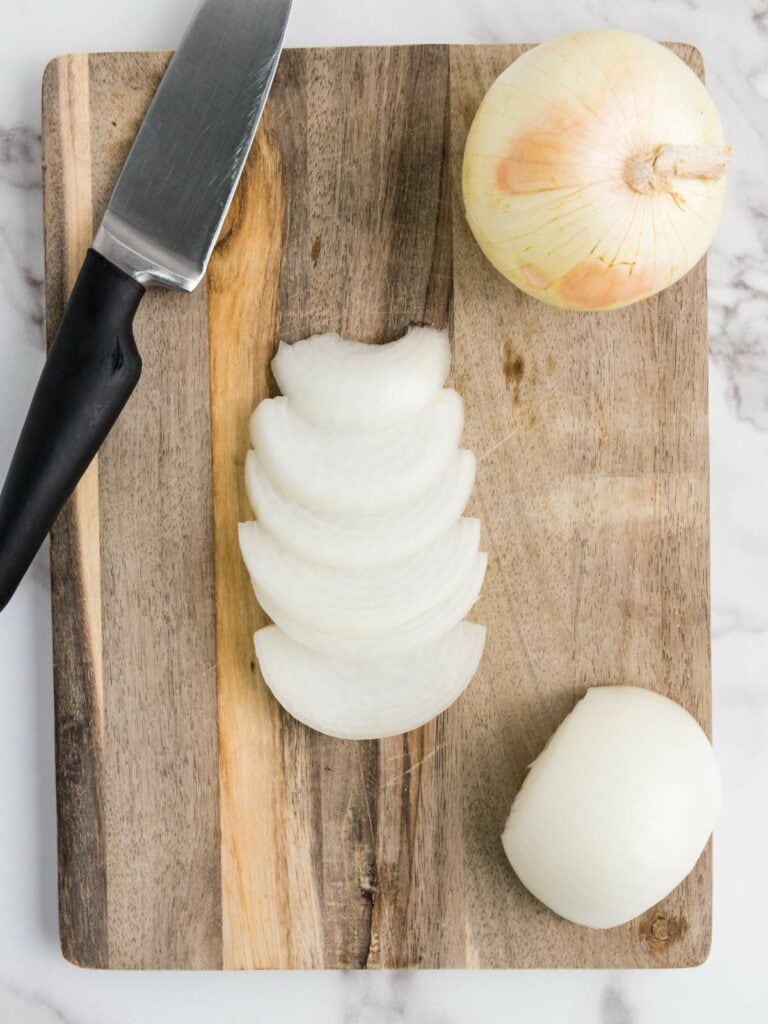 A knife and sliced onion on a wooden cutting board, with a whole onion nearby.