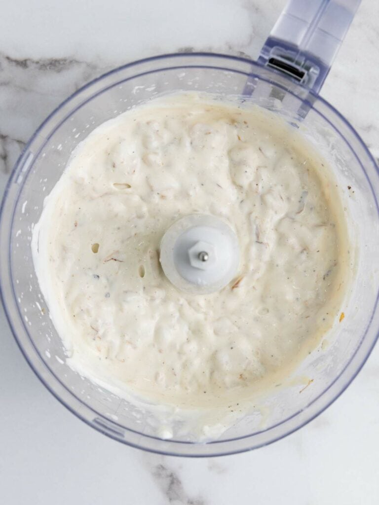 Overhead view of a food processor containing a creamy, textured mixture on a marble surface.