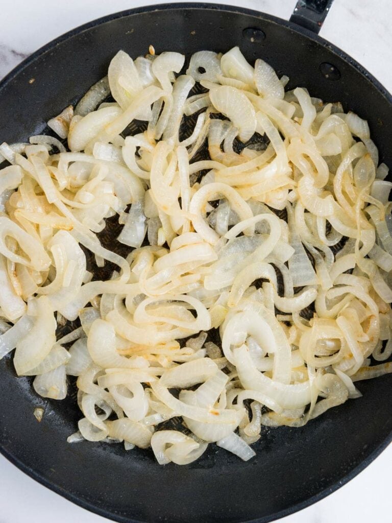 Sliced onions cooking in a black skillet on a stovetop.