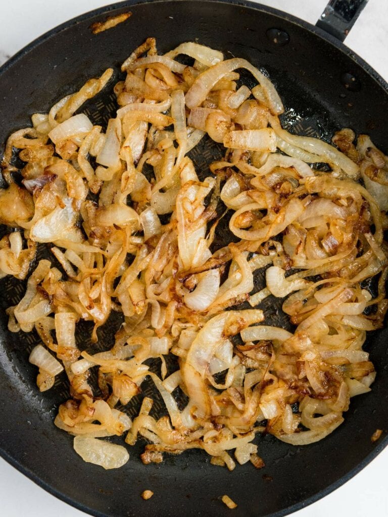 Caramelized onions in a black frying pan, evenly spread and golden brown, with a textured bottom visible.