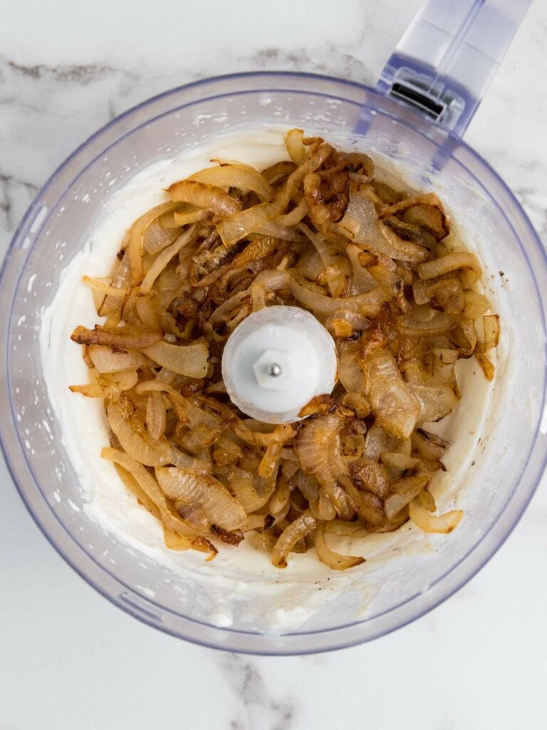 Caramelized onions in a food processor on a marble countertop.