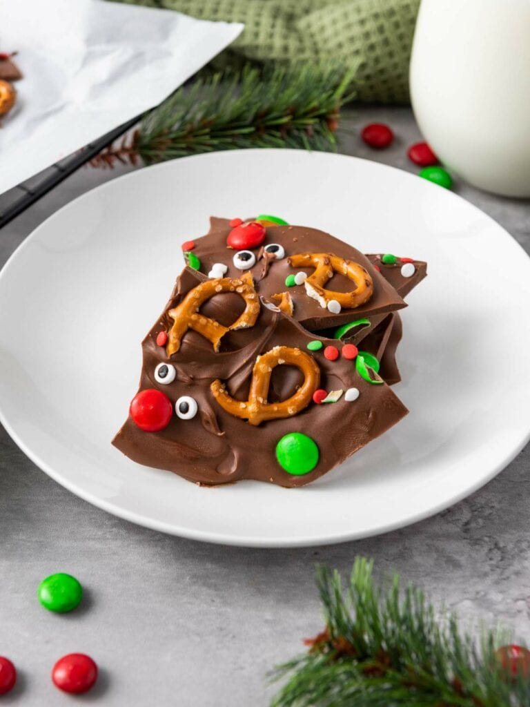 White plate with reindeer chocolate bark set on a festive table and a glass of milk nearby.