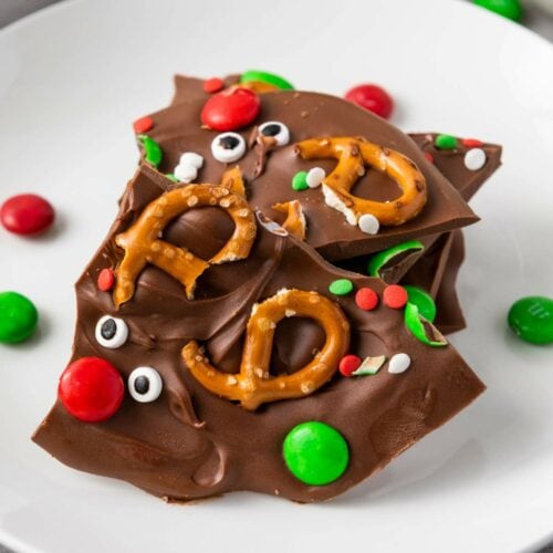 Reindeer chocolate bark with pretzels, festive sprinkles, and colorful candies on a white plate.