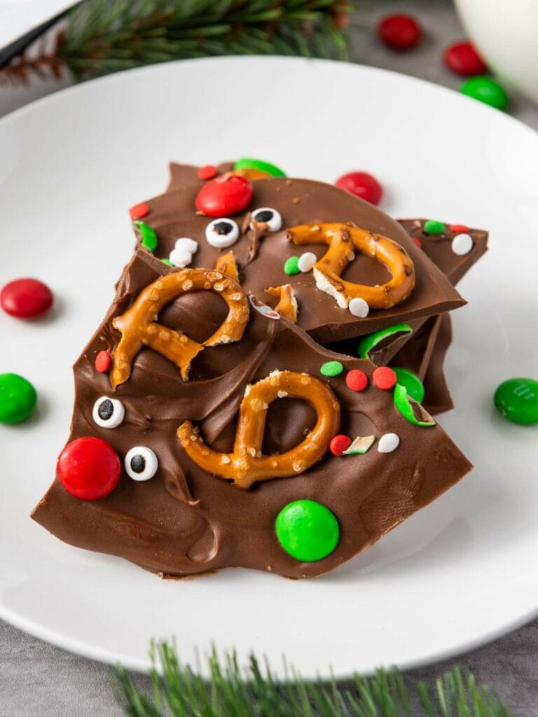 Reindeer chocolate bark with pretzels, festive sprinkles, and colorful candies on a white plate.