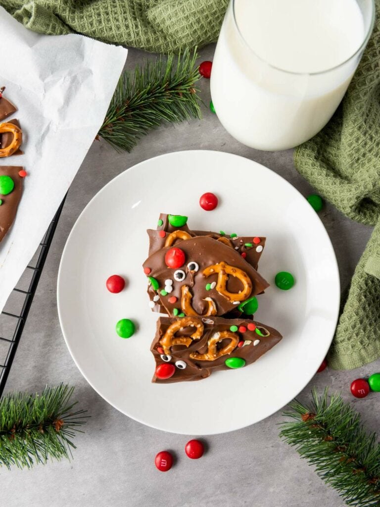 A plate with reindeer chocolate bark next to a glass of milk.